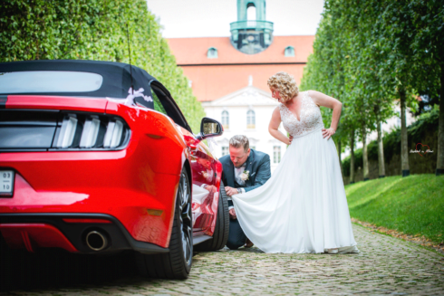 Bräutigam putzt sein Auto mit dem Brautkleid