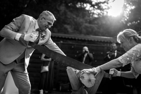 Hochzeitsfotografie - Brautpaar bei der Hochzeit im Kloster Nimbschen bei Grimma sägt den Baumstamm